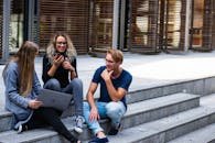 Three young professionals having a friendly chat while sitting on outdoor steps.