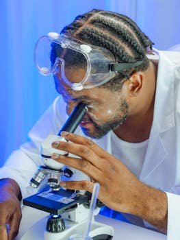 A scientist using a microscope in a laboratory setting with safety goggles.