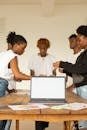 Diverse young professionals brainstorming and collaborating around a laptop in a modern office setting.
